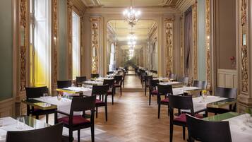 Ein langer, eleganter Speisesaal mit aufwendigen Wänden und Kronleuchtern, mit mehreren Tischen und Stühlen für das Abendessen.