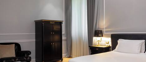 A hotel room with a large bed, a dark wooden wardrobe, a small table with a lamp, and a sofa.