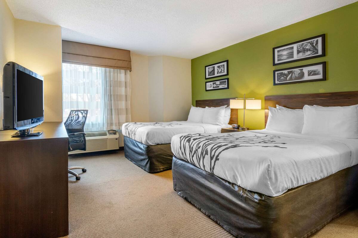 A hotel room with two beds, a desk with a television, a chair, and a window with curtains.