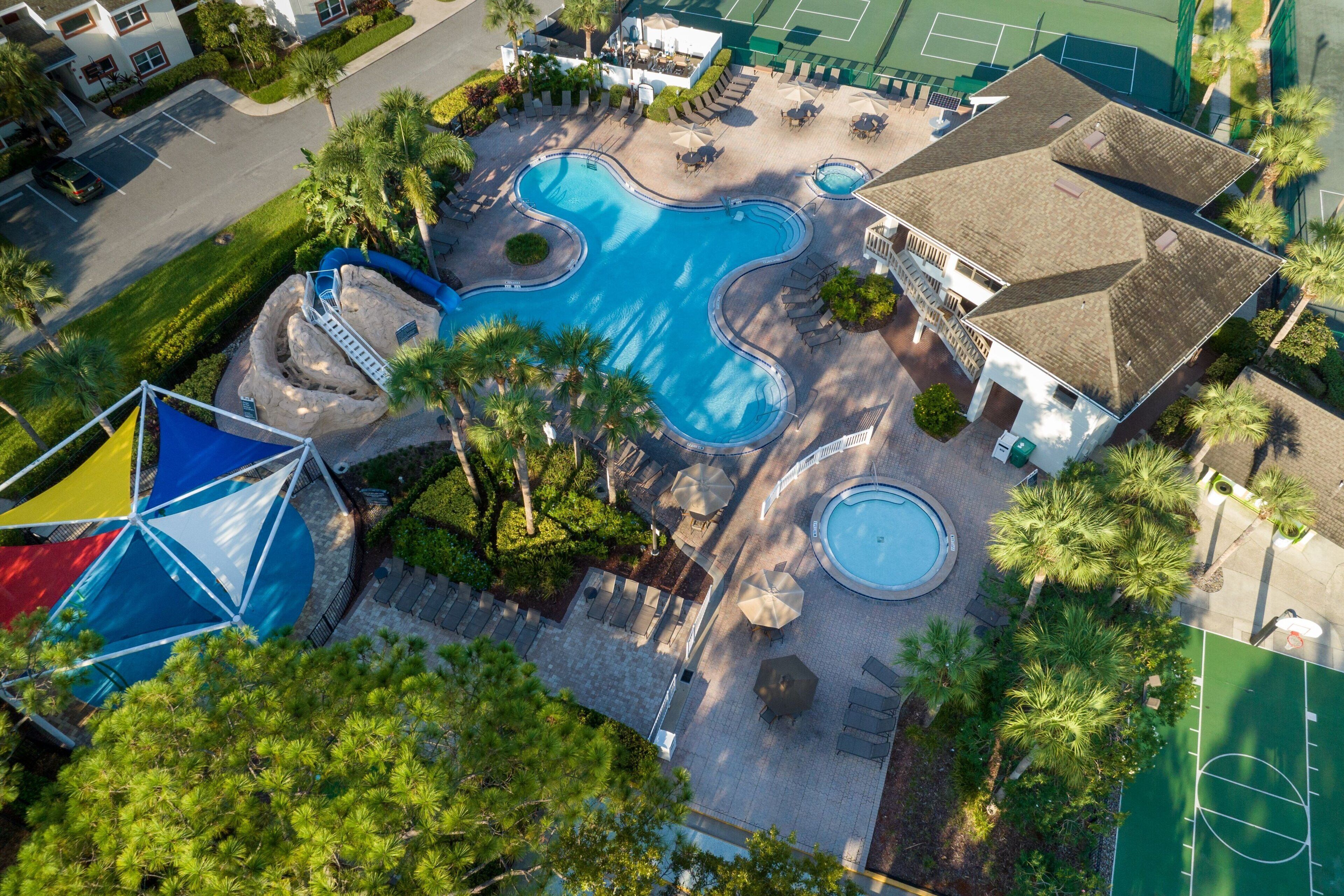 Vista aérea de un resort con varias piscinas, una cancha de tenis y zonas de estar al aire libre.