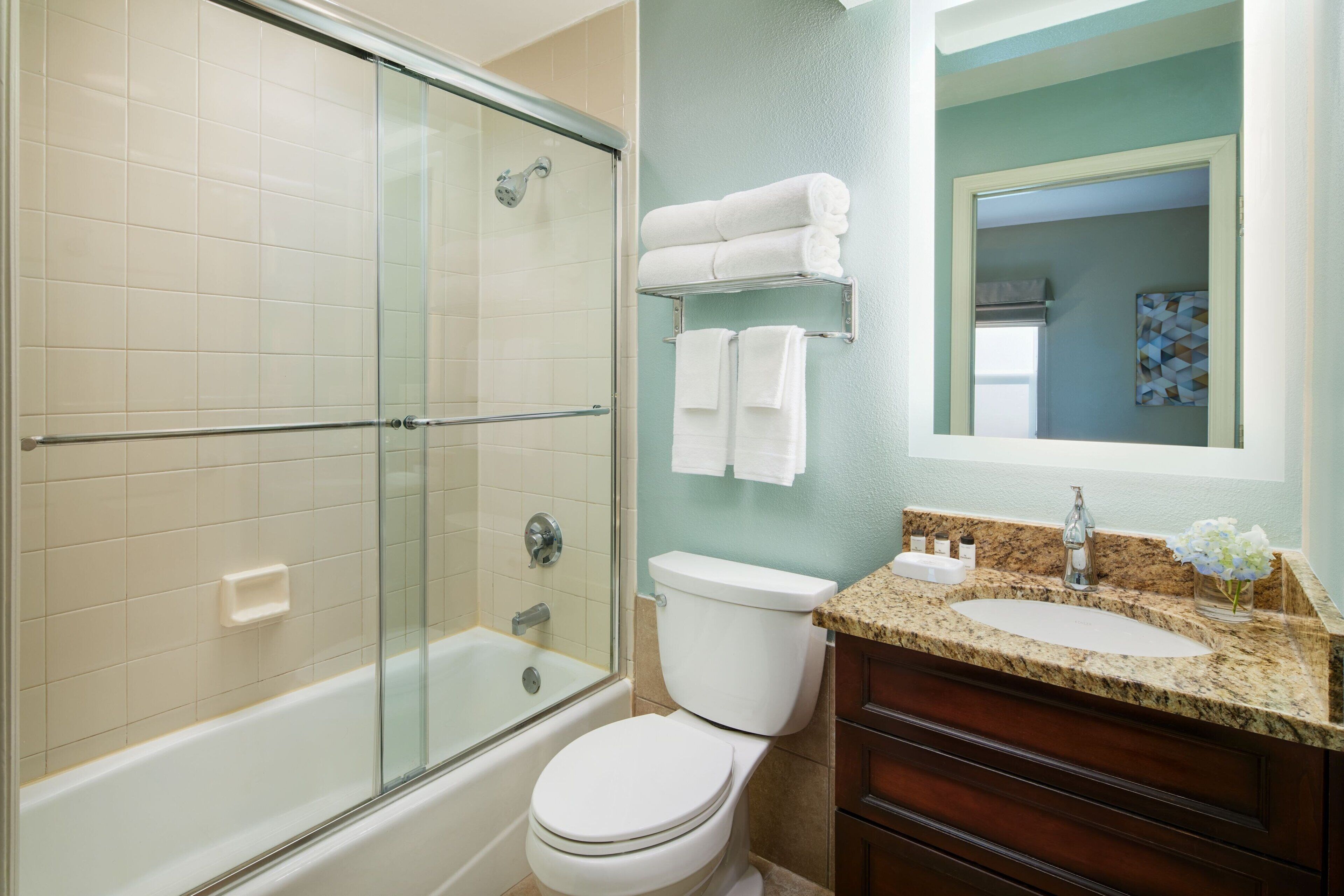 A bathroom with a glass-enclosed shower, a white toilet, a sink with a marble countertop, and a mirror above the sink.