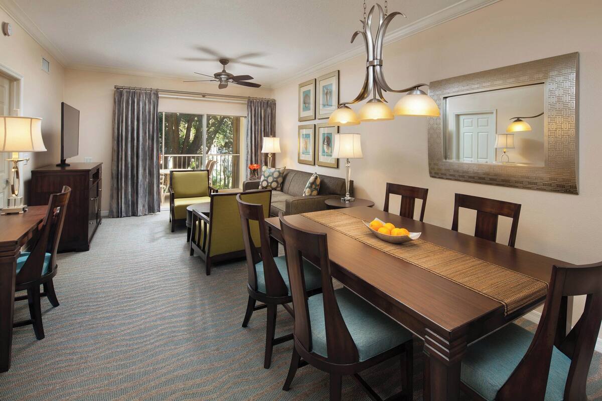 A hotel dining area with a wooden table, chairs, and a ceiling fan.