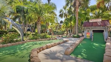 Un campo de minigolf con una escultura de delfín, palmeras y un letrero de tienda de barcos.