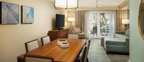Une chambre d’hôtel avec une table à manger en bois, des chaises, une télévision, un canapé et un balcon avec des rideaux.