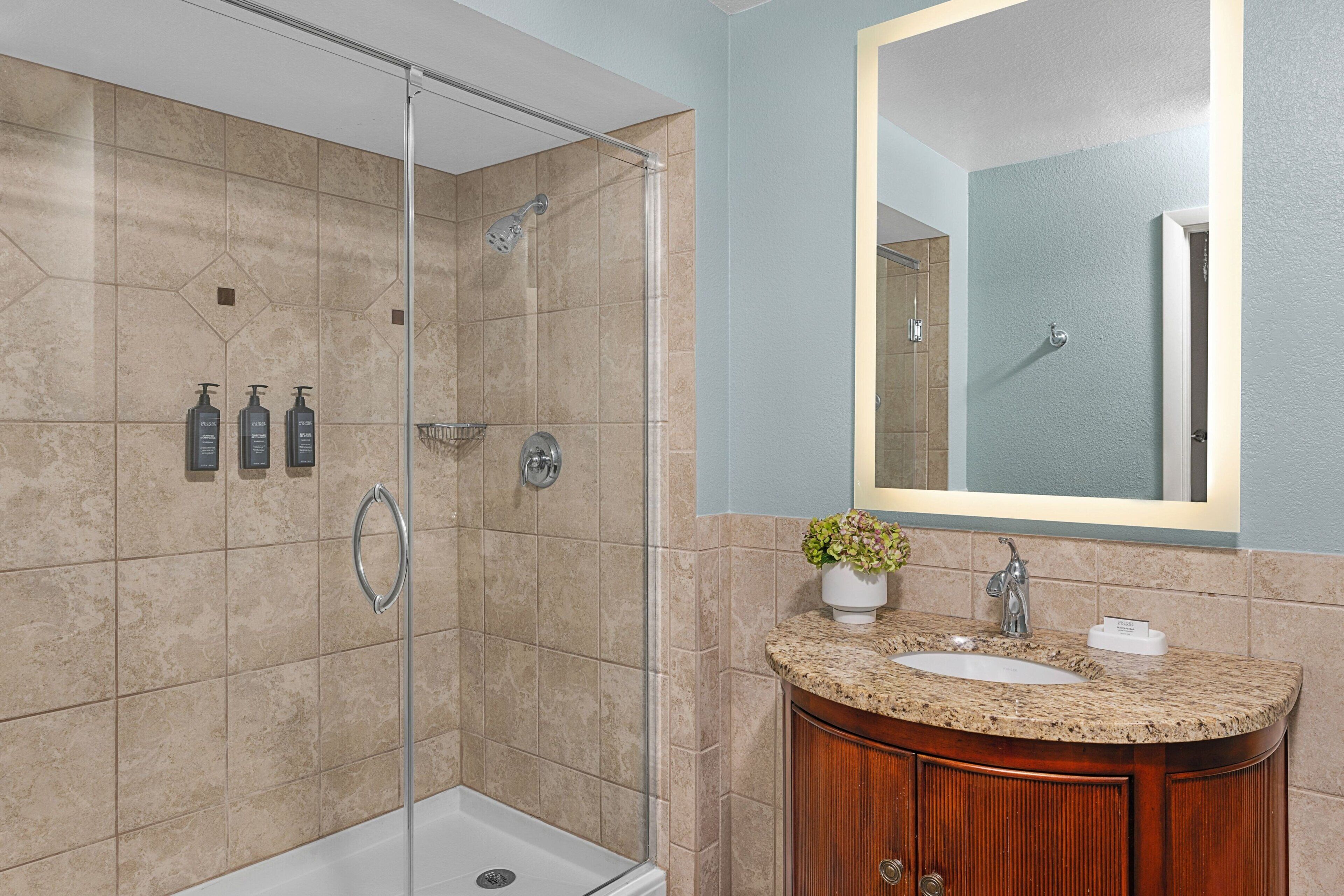 A modern bathroom with a glass-enclosed shower, a sink with a granite countertop, and a wooden vanity.