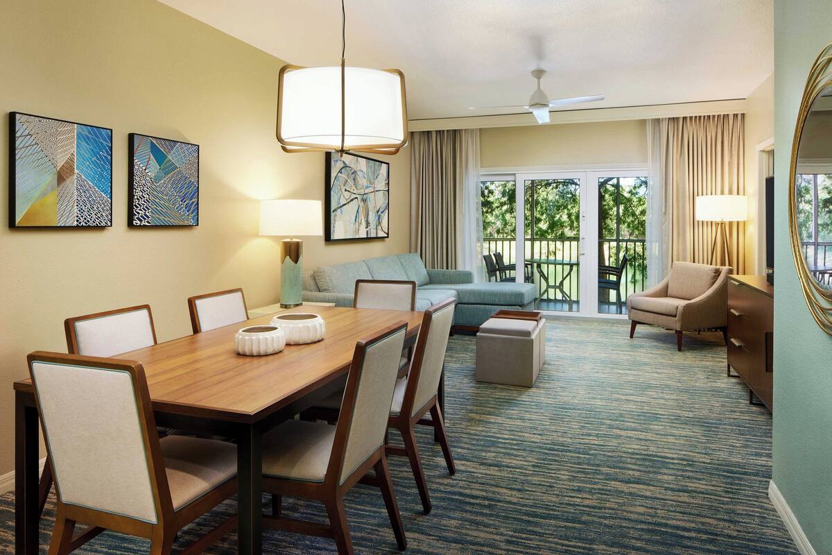 A hotel room with a dining area, a sofa, a chair, and a balcony with a view.