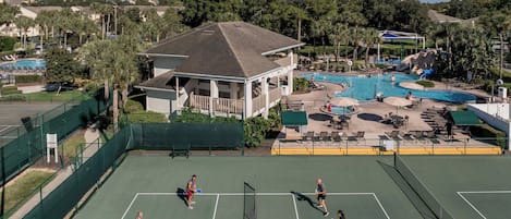A tennis court with a pool and water slide nearby.