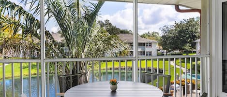 A covered outdoor area with a table and chairs, a view of a water body, and surrounding greenery.
