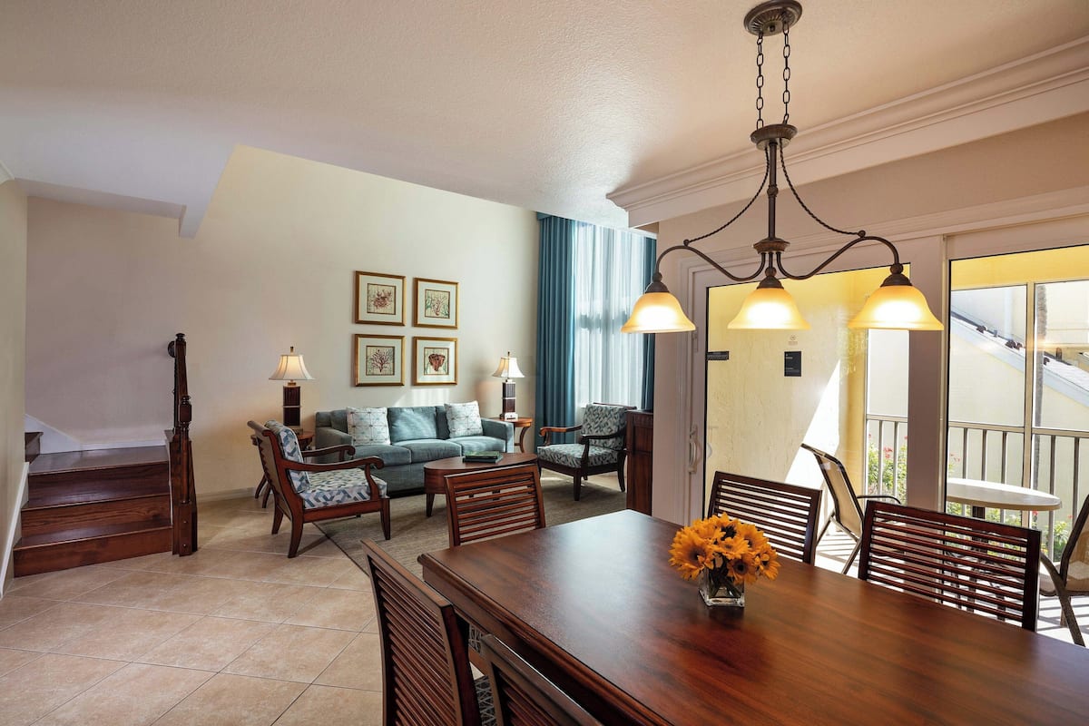 A dining area with a wooden table and chairs, a chandelier, and a staircase leading to another level.
