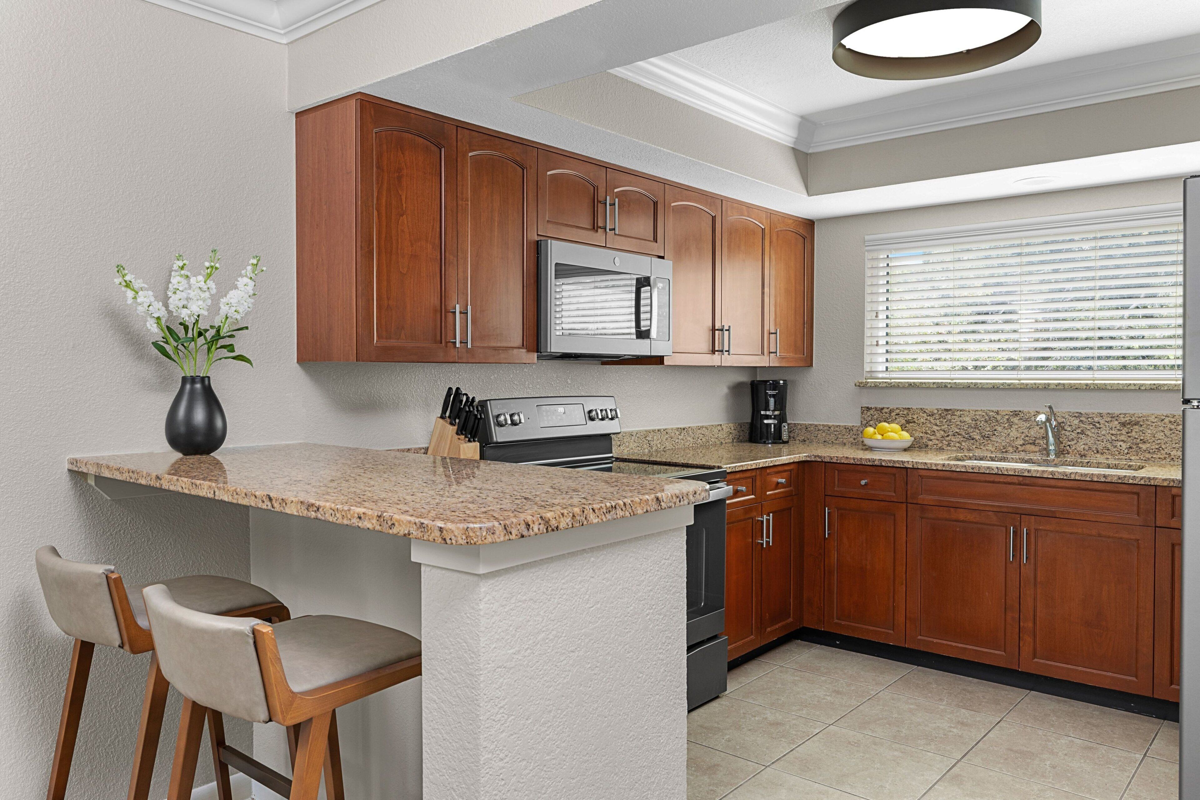 A kitchen with wooden cabinets, a granite countertop, a built-in oven, and a window with blinds.