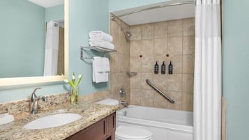 Une salle de bain avec deux lavabos, des toilettes, une baignoire et une douche équipée d’une barre d’appui.