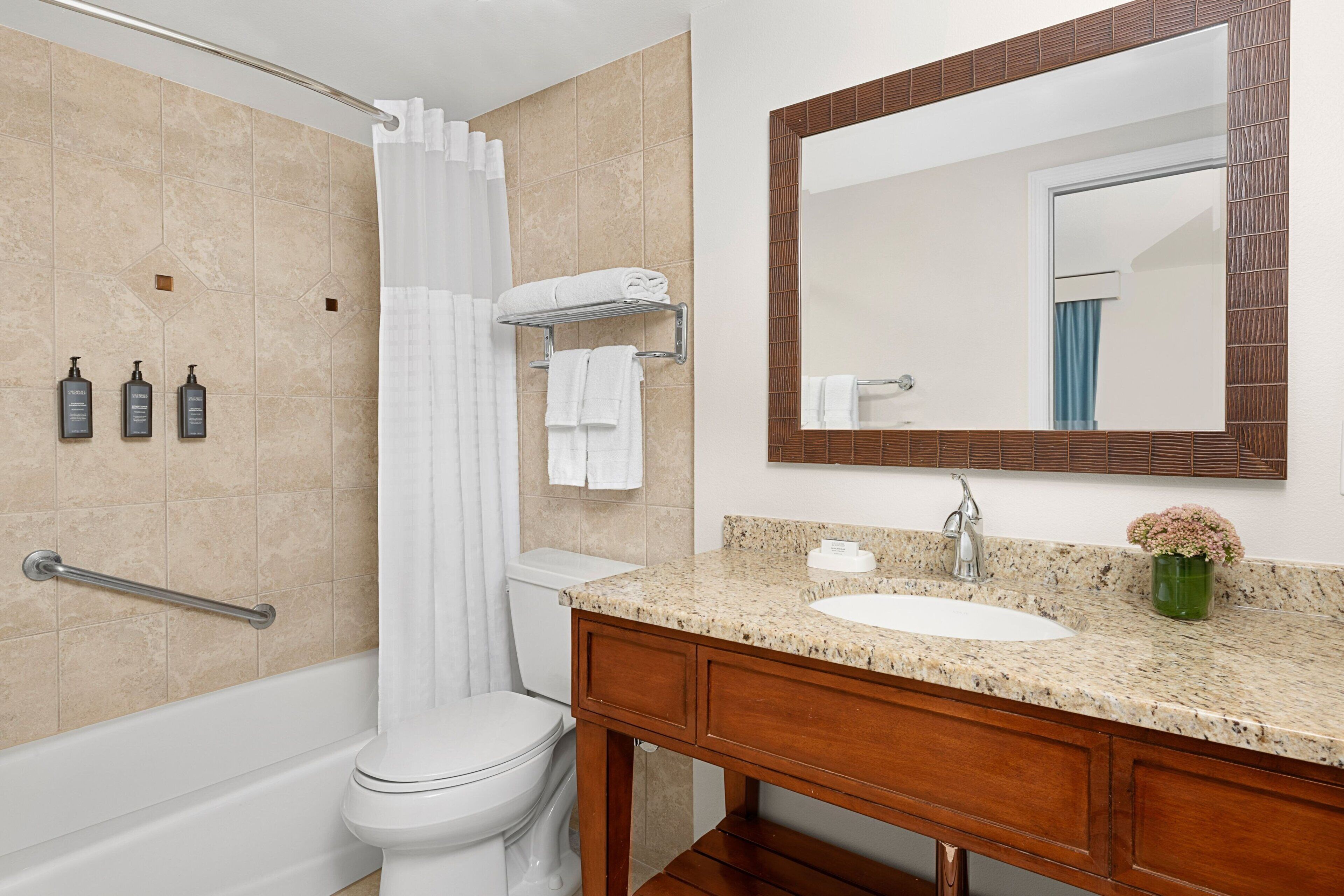 A bathroom with a bathtub, toilet, vanity with a sink, and a mirror.