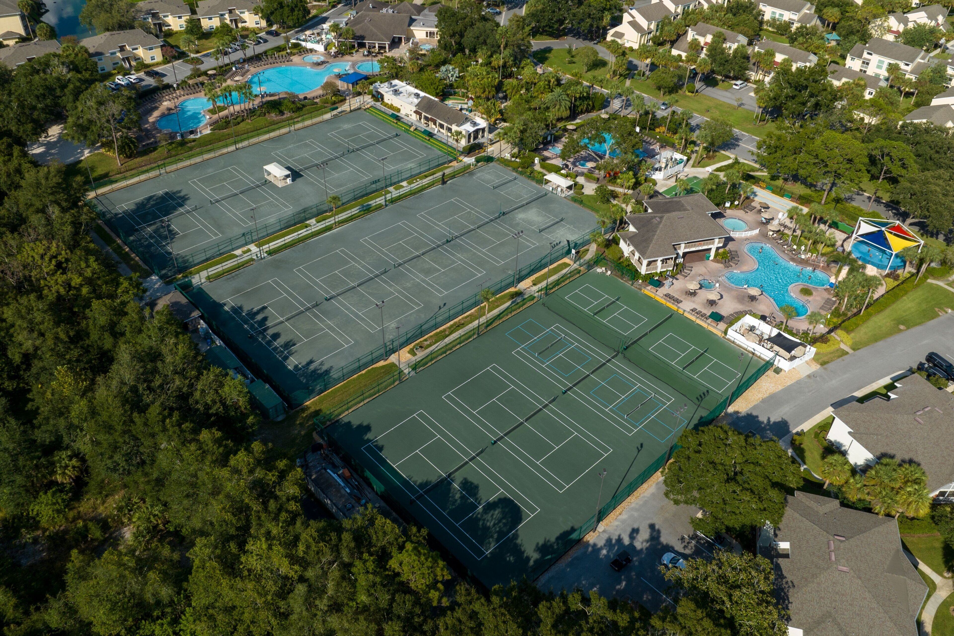 Vue aérienne d’un quartier résidentiel avec deux courts de tennis, une piscine et les maisons environnantes.