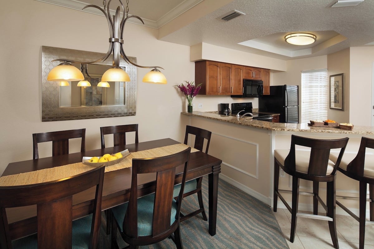 A modern kitchen with wooden cabinets, a central island, and a dining area with a wooden table and chairs.