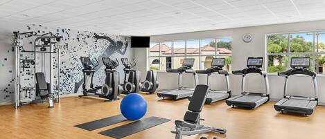 Un gimnasio con cintas de correr, elípticas y pesas libres.