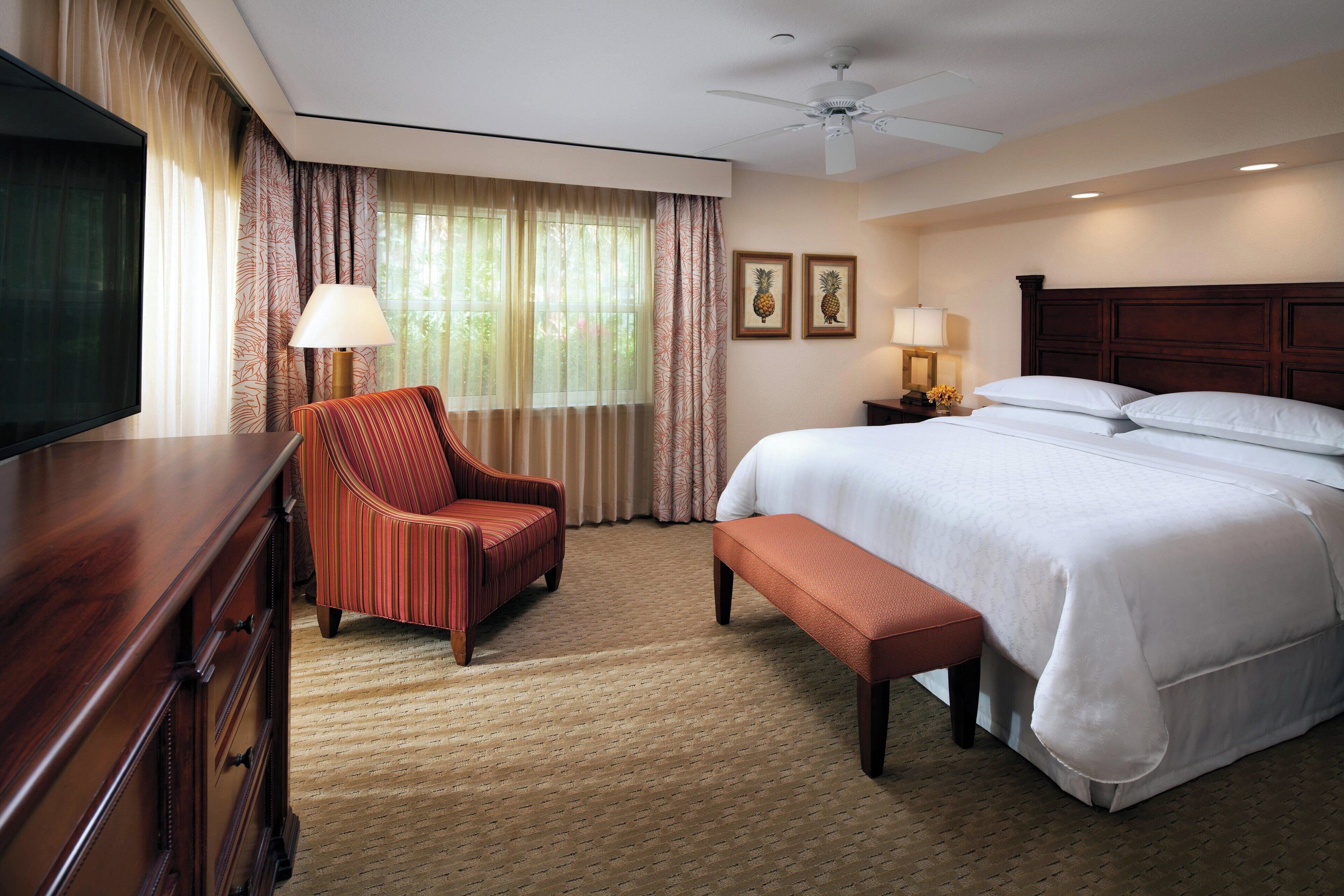 A hotel room with a bed, a chair, a desk, a television, and a ceiling fan.