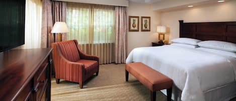 A hotel room with a bed, a chair, a desk, a television, and a ceiling fan.