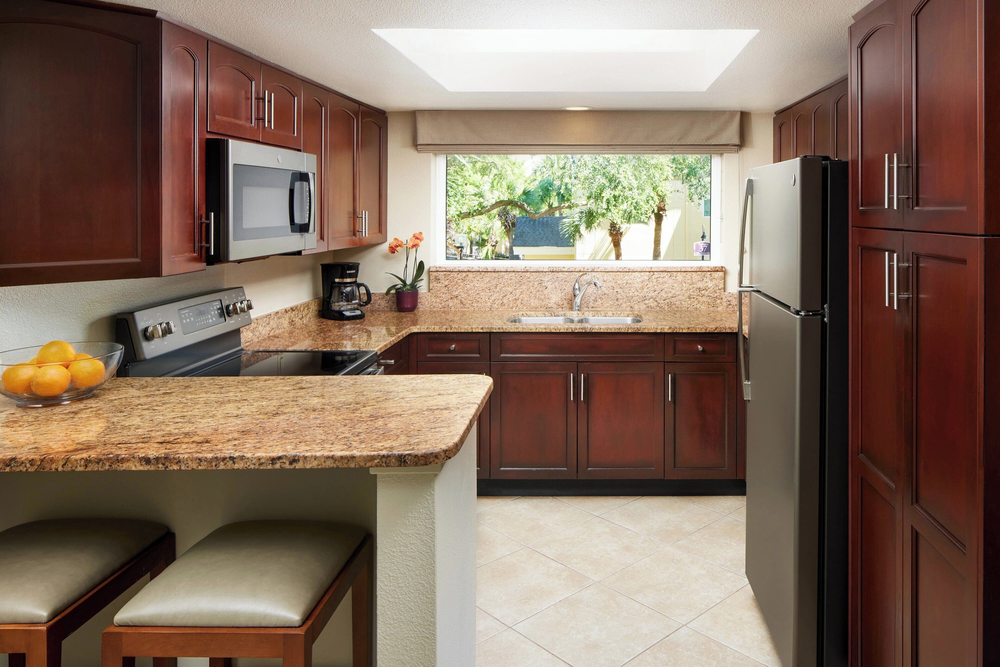 A modern kitchen with dark wood cabinets, a granite countertop, a built-in microwave, a stainless steel sink, and a refrigerator.