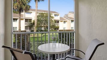 A balcony with a round table and two chairs, overlooking a residential area with apartment buildings and a lawn.