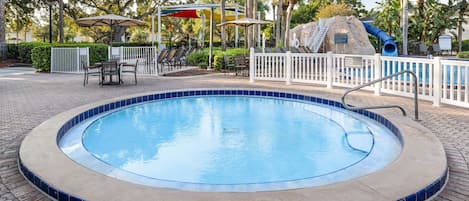 A circular pool with a tiled edge, surrounded by a white fence, and a water slide in the background.