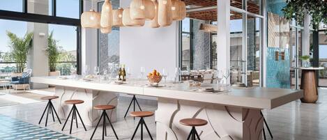 Una cocina moderna con una isla grande, taburetes de bar, lámparas de ratán colgantes y ventanas amplias.