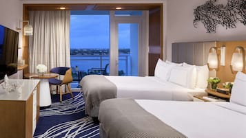 A hotel room with two beds, a desk, a chair, a small table, and a view of the city.