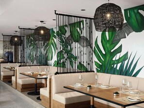 A modern dining area with booths and tables, featuring a tropical leaf mural and hanging black lamps. - Hilton Fort Lauderdale Marina (Fort Lauderdale)