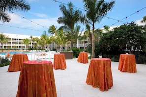 An outdoor area with tables covered in orange tablecloths, a pool, and palm trees.