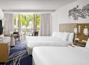 Habitación de hotel con dos camas, un escritorio, una silla, televisión y vistas a palmeras.