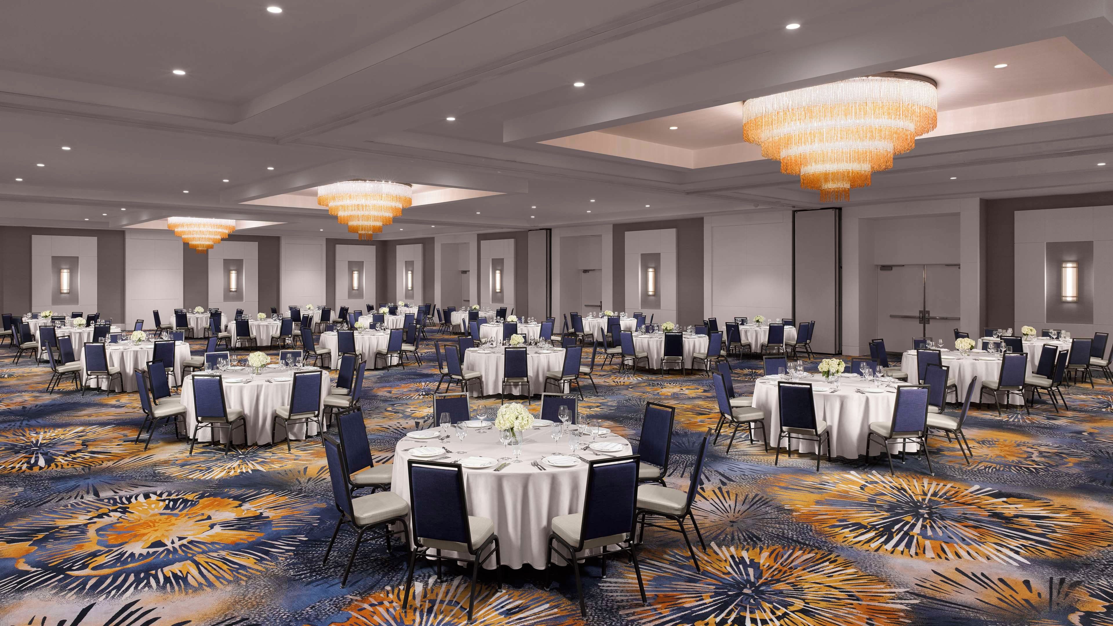 A large banquet hall with round tables, blue chairs, and a patterned carpet.