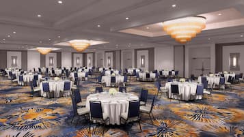 Un gran salón de banquetes con mesas redondas, sillas azules y una alfombra estampada.