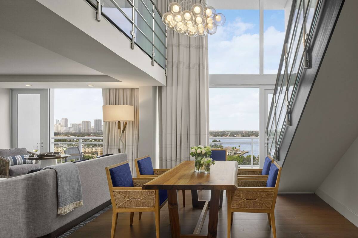 A modern living room with a dining area, large windows, and a view of the city skyline.