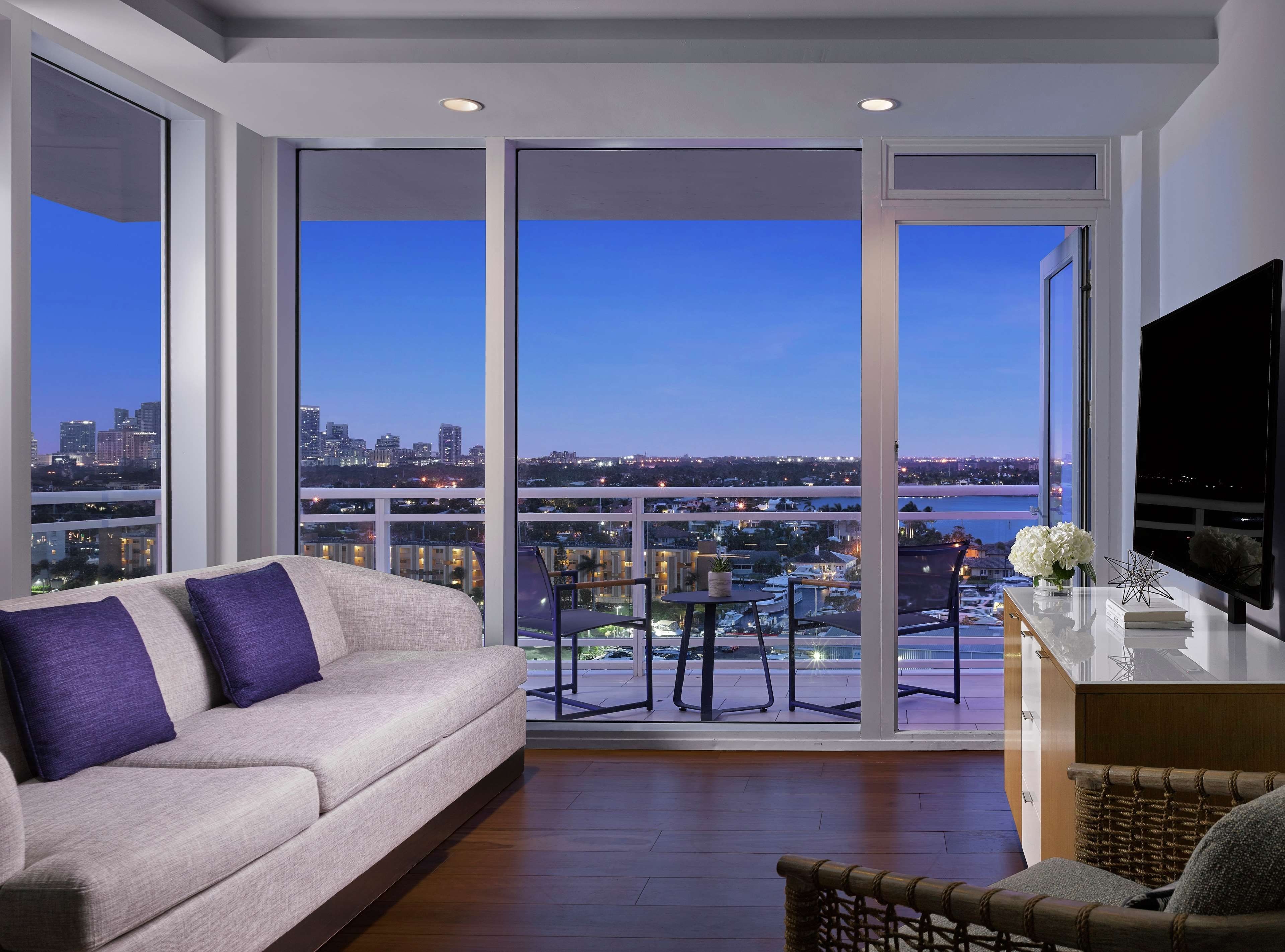 A modern living room with a sofa, a TV, and a balcony with a city view.