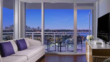 A modern living room with a sofa, a TV, and a balcony with a city view.