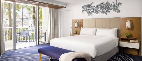 A hotel room with a large bed, a bench, a nightstand, and a wall-mounted lamp.