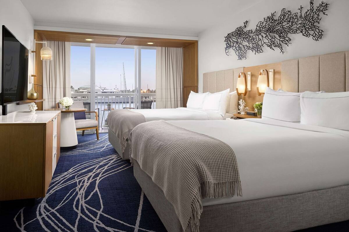 A hotel room with a large bed, a desk, a TV, and a view of the city.