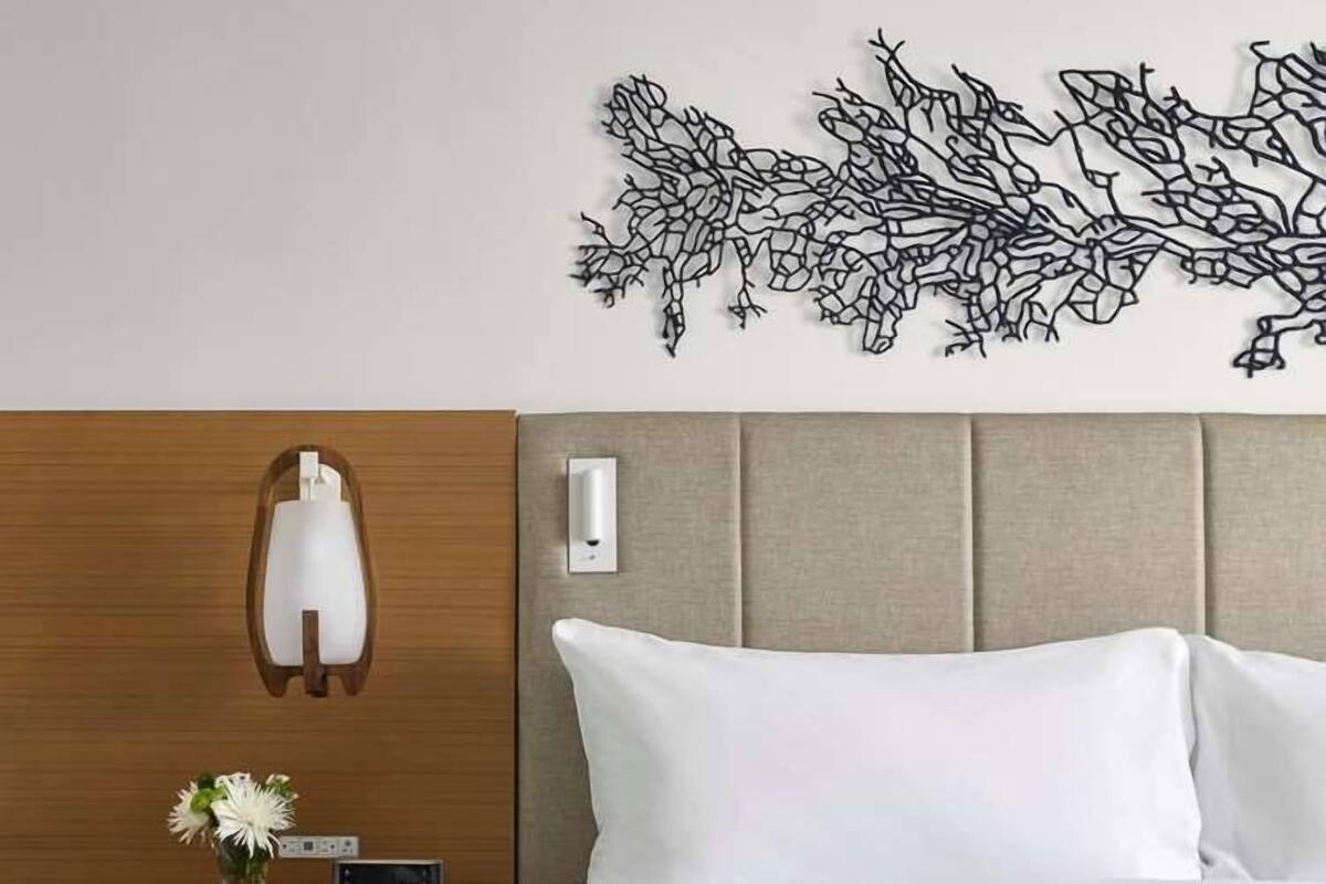 A hotel room with a bed, a nightstand with a lamp, a wall art piece, and a vase with flowers.