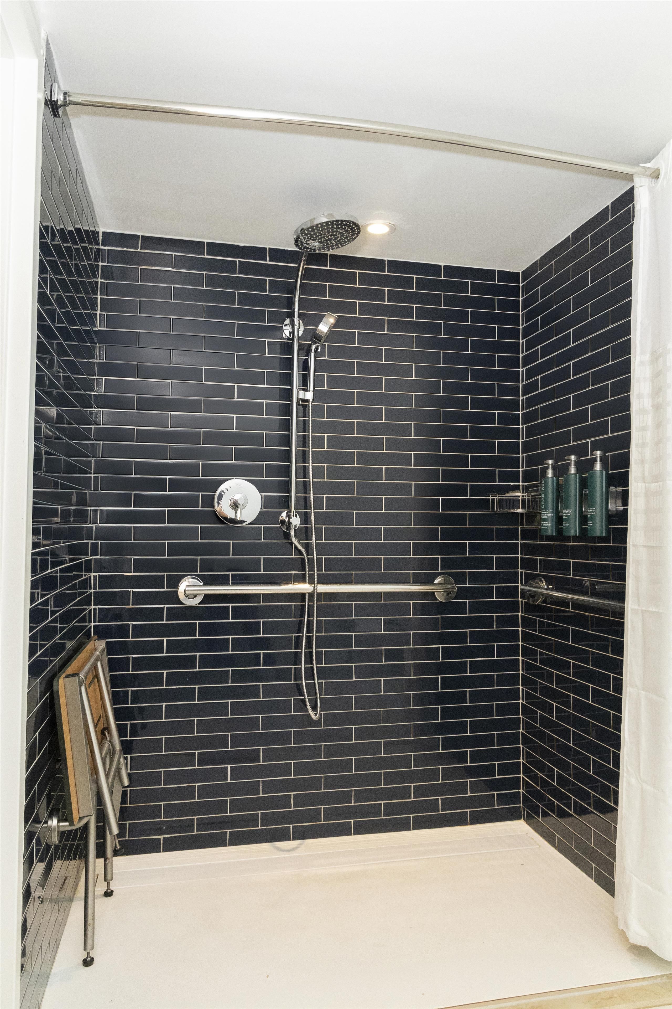 A shower with black tiled walls, a glass door, and a metal grab bar.
