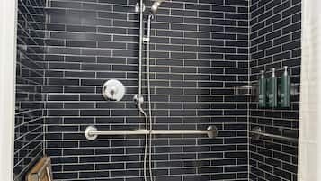 Een douche met zwart betegelde wanden, een glazen deur en een metalen handgreep.