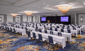 A large conference room with rows of tables and chairs, a stage with a screen, and chandeliers. - Hilton Fort Lauderdale Marina (Fort Lauderdale)