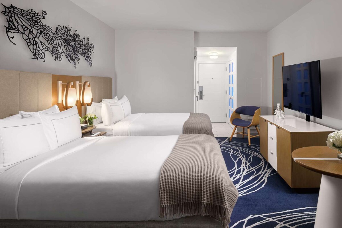 A hotel room with two beds, a desk, a TV, and a decorative wall piece.