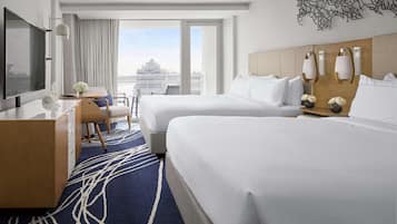 A hotel room with two beds, a desk, a TV, and a large window with a view of a cruise ship.