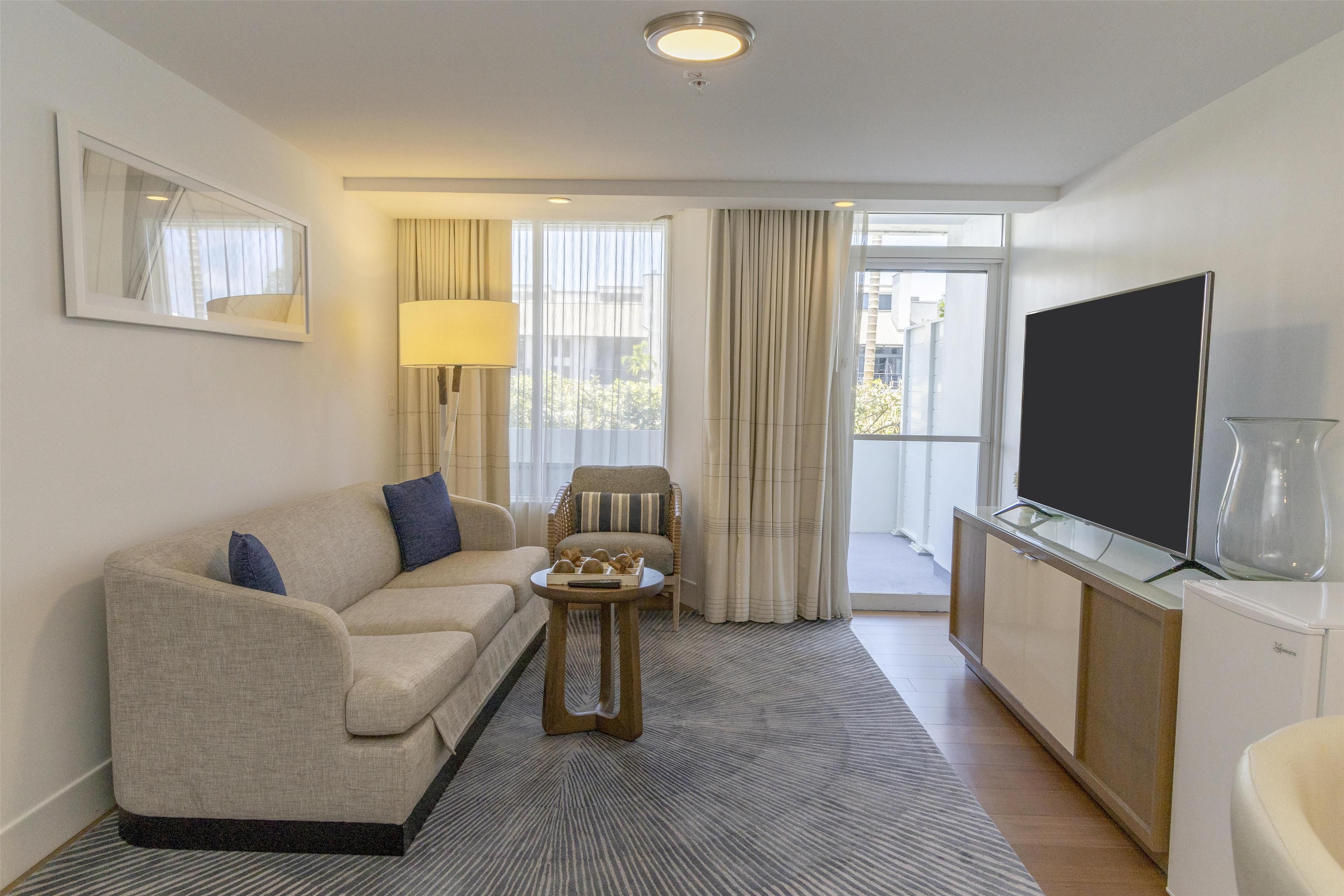 A modern hotel room with a sofa, a small side table, a television, and a glass cabinet.