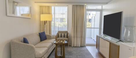 A modern hotel room with a sofa, a small side table, a television, and a glass cabinet.