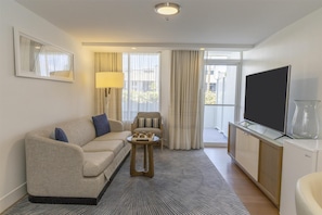 A modern hotel room with a sofa, a small side table, a television, and a glass cabinet.