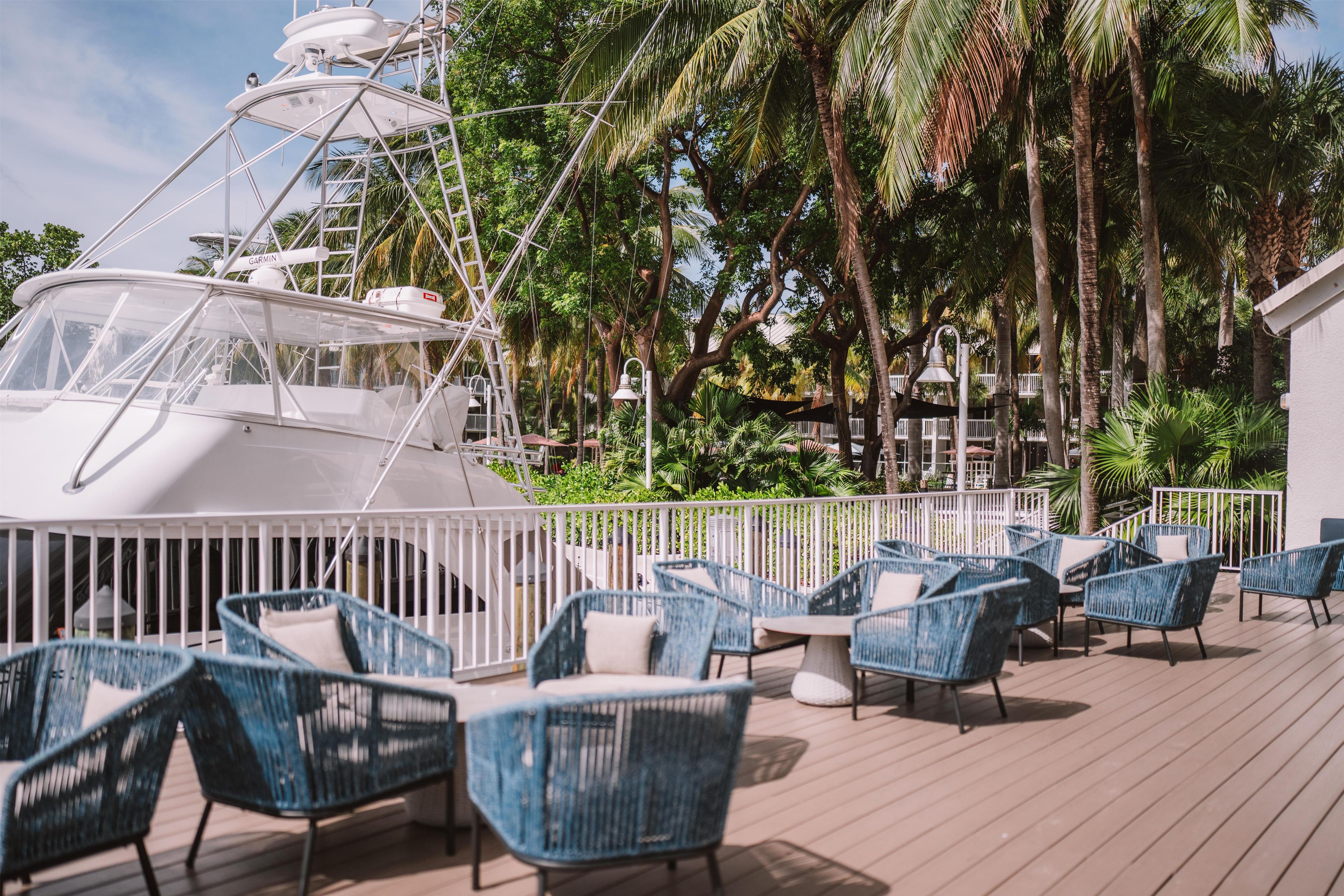 Un yacht est amarré sur une plateforme dotée d’un espace salon extérieur, avec des palmiers en arrière-plan.