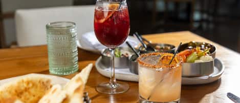 Una mesa de comedor con pan plano, un vaso de bebida roja con una rodaja de limón, una margarita con borde de sal y un vaso verde.