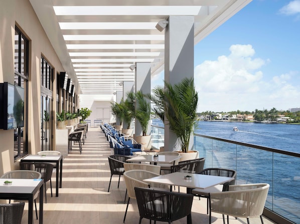 A sunlit outdoor seating area with tables and chairs, overlooking a body of water. - Hilton Fort Lauderdale Marina (Fort Lauderdale)