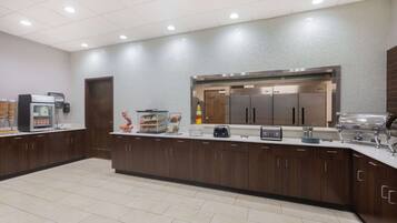 A modern kitchen with a central island, equipped with a coffee machine, toaster, and food display.