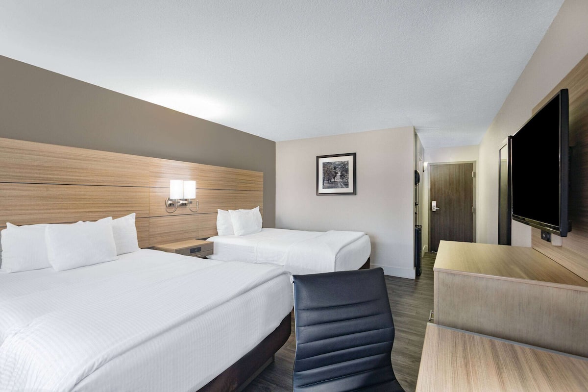 A hotel room with two beds, a TV, a desk, and a chair.